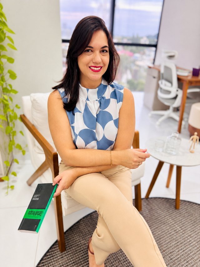 Suelen Silva sentada em seu consultório em Joinville, segurando um livro de Gestalt-terapia